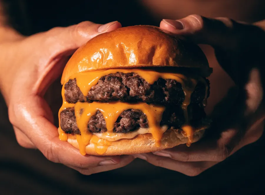 Un double smash burger au cheddar coulant tenu à deux mains